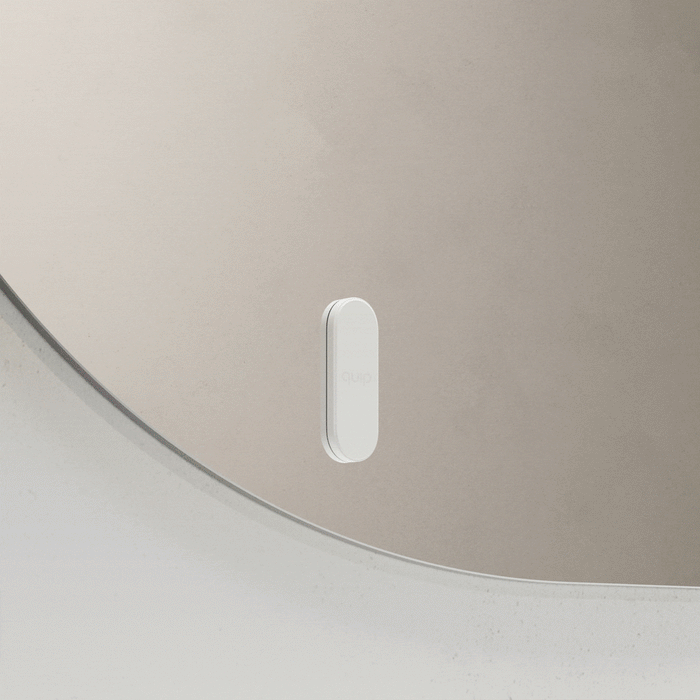 White quip toothbrush mount attaching to and releasing from a bathroom mirror.