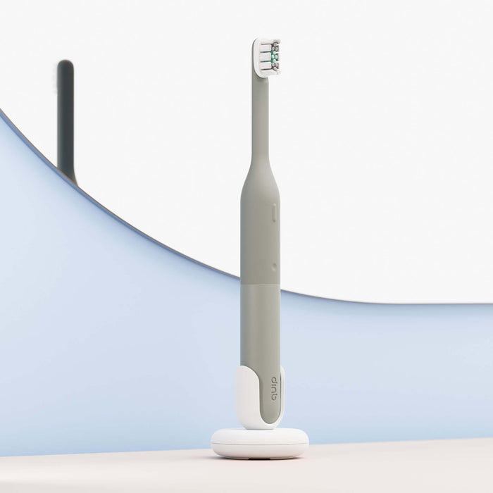Gray electric toothbrush on a white stand with a blurred background
